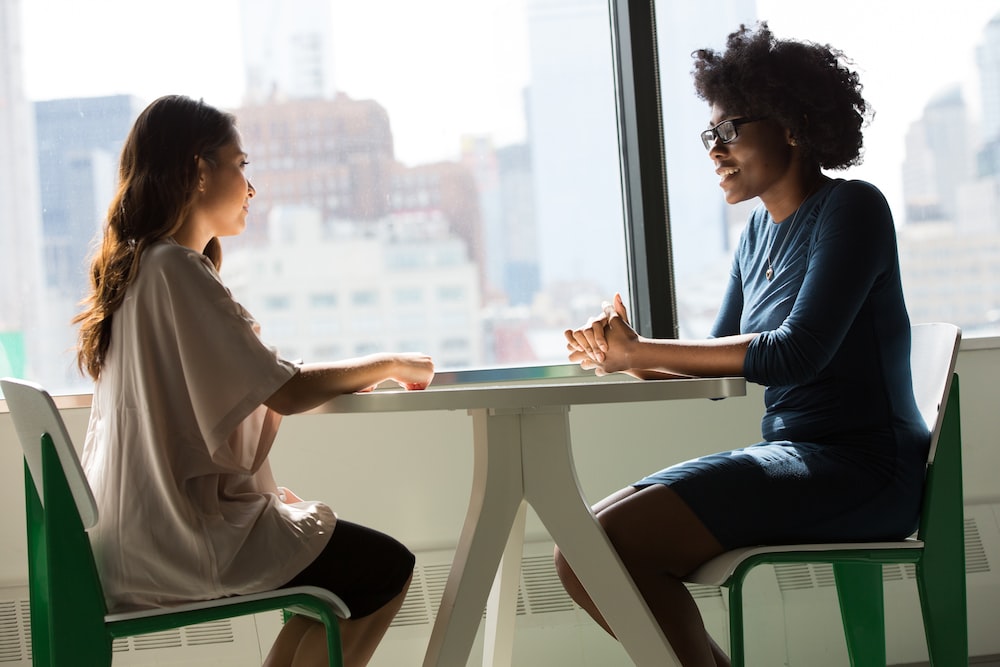two women sitting beside table and talking about remote closing jobs